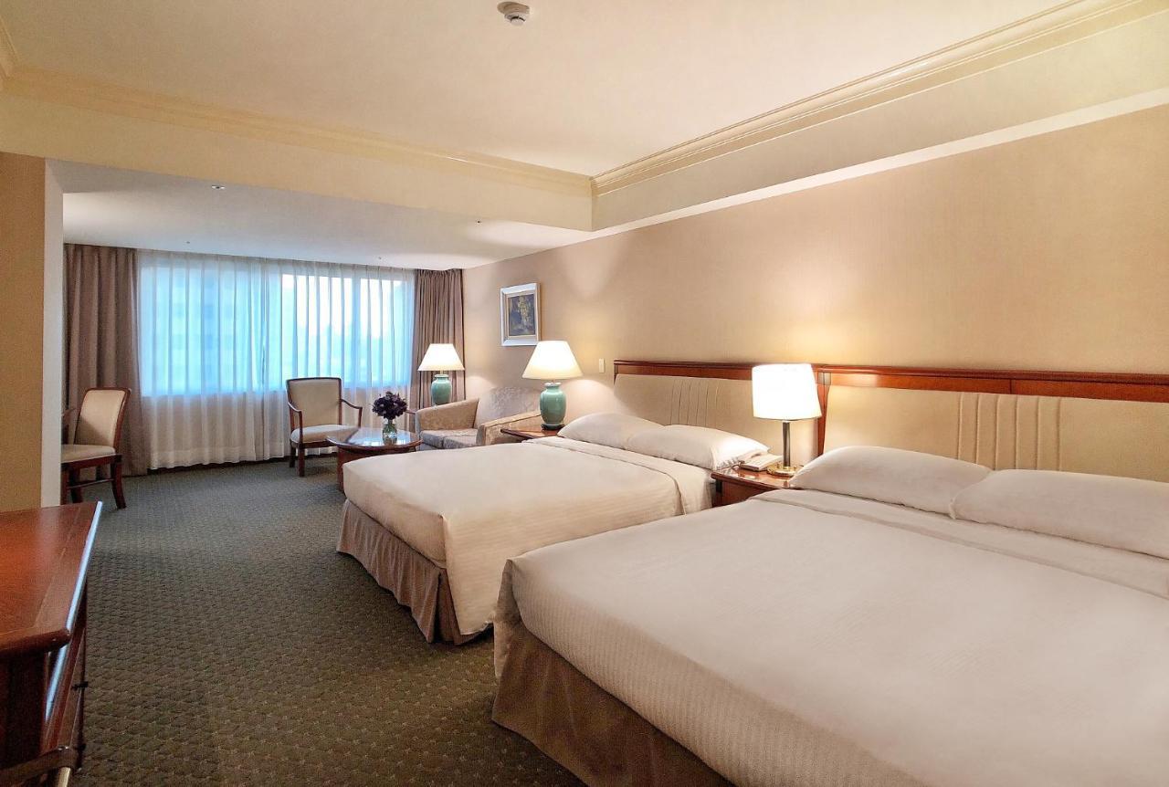 Evergreen Laurel Hotel - Тайчжун Экстерьер фото The photo shows a hotel room featuring two queen-sized beds with white linens. The room is well-lit and has a warm, neutral color palette. There are bedside lamps on each side of the beds and a small table. To the side, there's a comfortable armchair