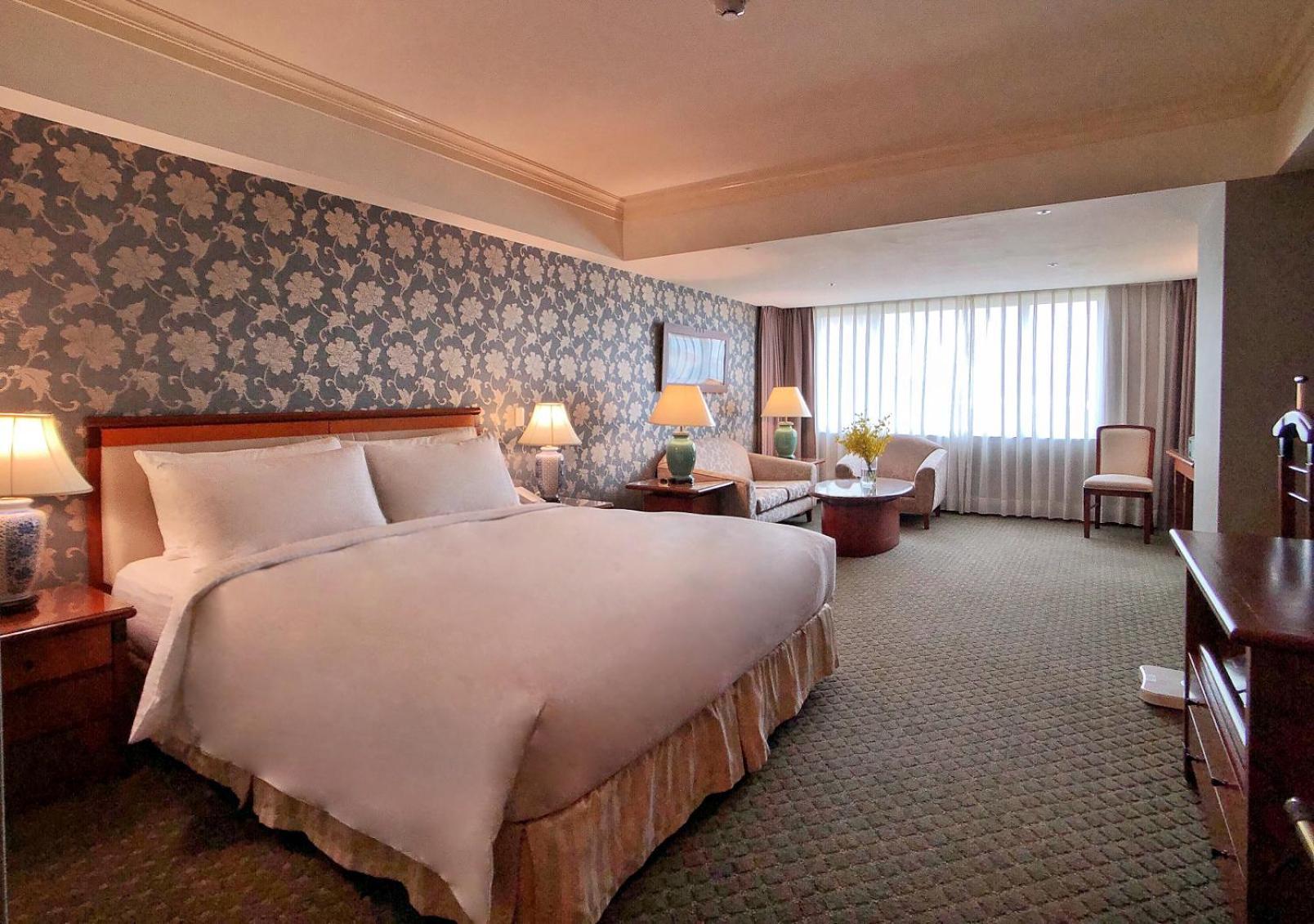 Evergreen Laurel Hotel - Тайчжун Экстерьер фото The photo shows a hotel room with a spacious and comfortable layout. It features a large bed with white bedding, placed against a decorative wallpapered wall. On either side of the bed, there are lamps providing soft lighting. In addition to the bed,