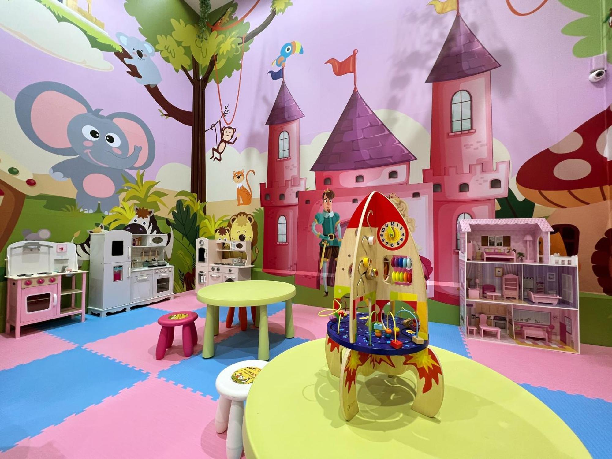 Evergreen Laurel Hotel - Тайчжун Экстерьер фото The photo shows a colorful children's playroom designed with a whimsical theme. The walls are painted in bright colors and feature a cartoon-style mural of a pink castle with purple towers and a smiling cartoon elephant. The room is filled with playf
