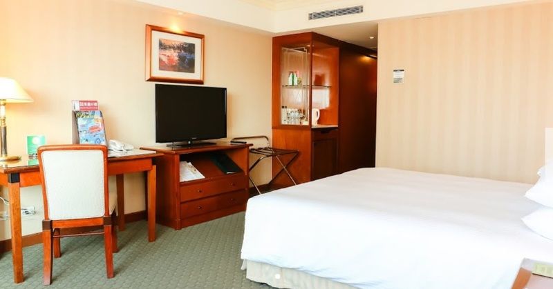 Evergreen Laurel Hotel - Тайчжун Экстерьер фото The photo shows a hotel room featuring a neatly made bed with a white blanket. On one side, there is a wooden desk with a chair, and a flat-screen television is mounted nearby. An accent cabinet is visible, displaying various items. The walls are pai