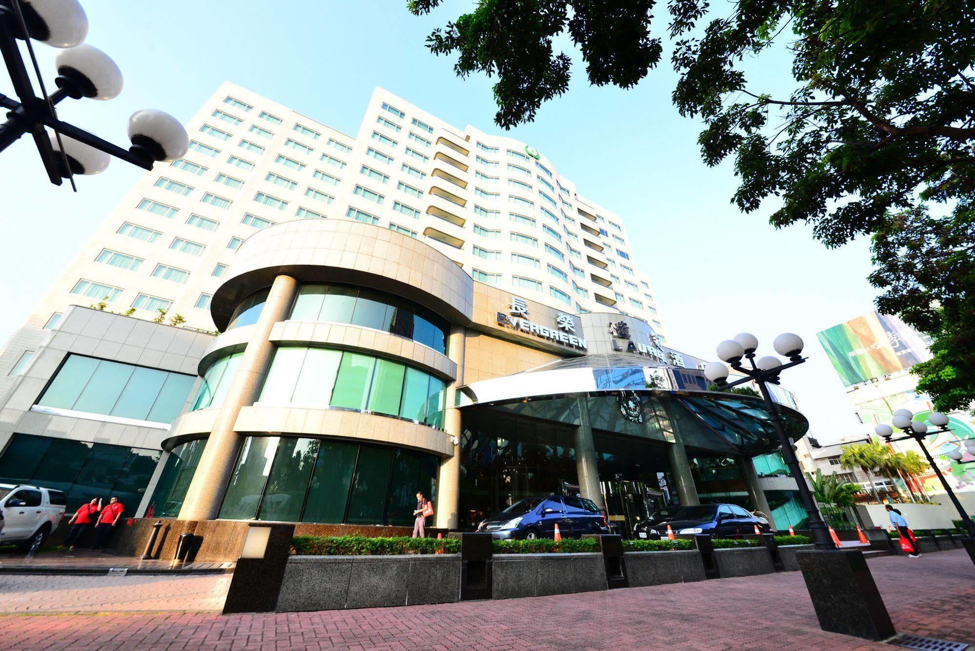 Evergreen Laurel Hotel - Тайчжун Экстерьер фото The photo shows a modern multi-story building, which appears to be a hotel or commercial establishment. The structure has a rounded glass entrance with a distinctive architectural design, featuring large windows. The building is surrounded by greener