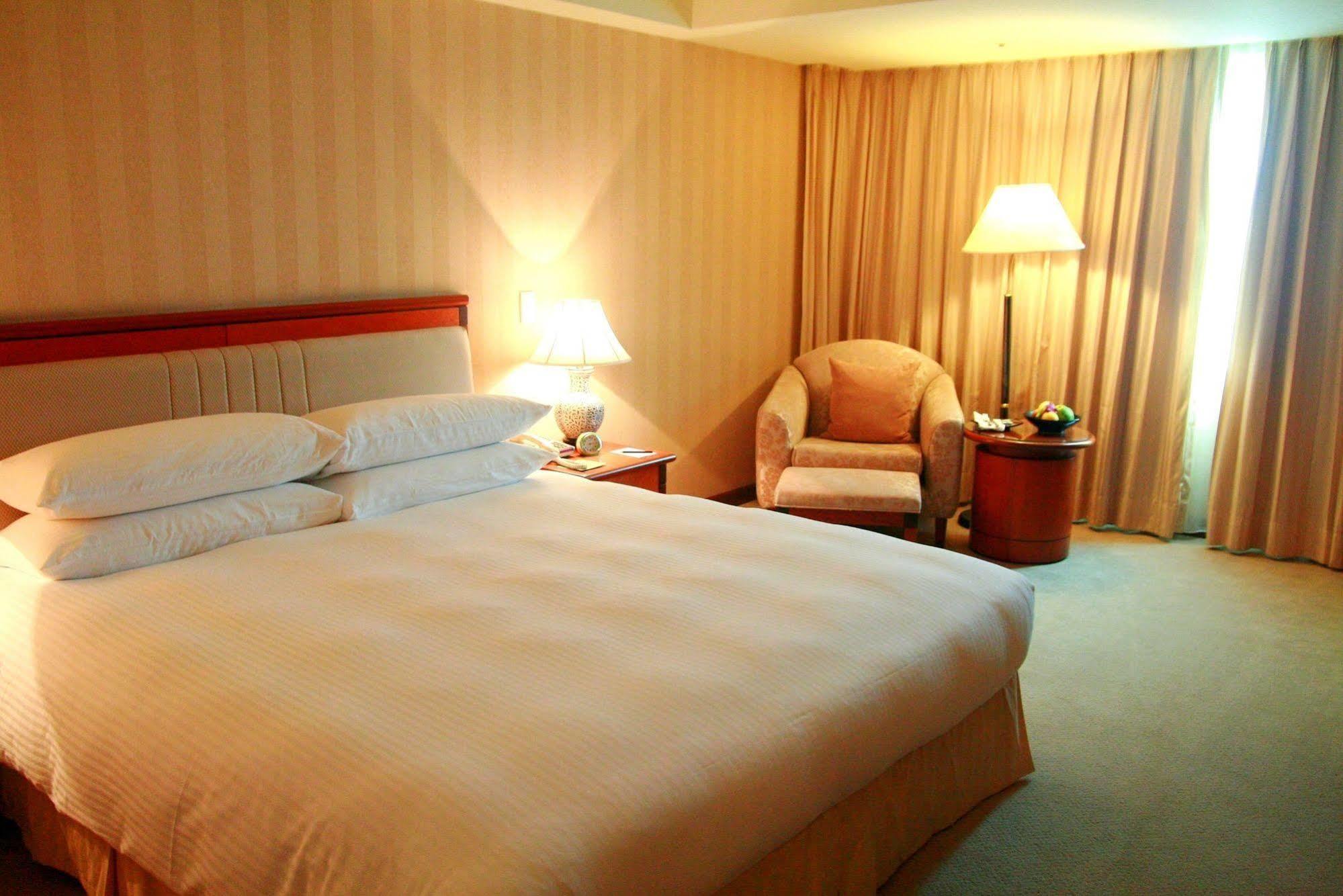 Evergreen Laurel Hotel - Тайчжун Экстерьер фото The photo shows a hotel room containing a large bed with white linens, flanked by two bedside lamps. To one side, there is a cozy armchair and a small side table with a fruit bowl or snacks. The walls are decorated in a soft, neutral color, and there