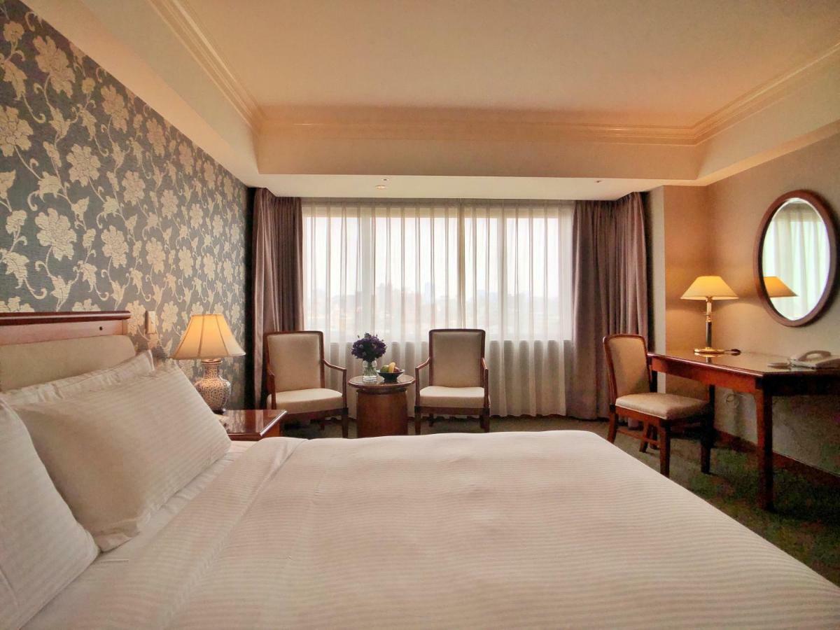 Evergreen Laurel Hotel - Тайчжун Экстерьер фото The photo shows a hotel room with a comfortable and inviting design. There is a large bed with crisp white bedding on the left side of the image. To the right, there are two elegant chairs with a small round table between them, adorned with a bouquet