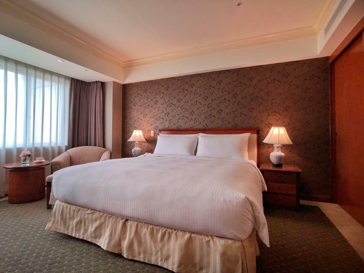 Evergreen Laurel Hotel - Тайчжун Экстерьер фото The photo shows a neatly arranged hotel room featuring a large bed with white linens and a light-colored bed skirt. On either side of the bed, there are small wooden nightstands with lamps. To the left of the bed, there's a comfortable chair and a ro