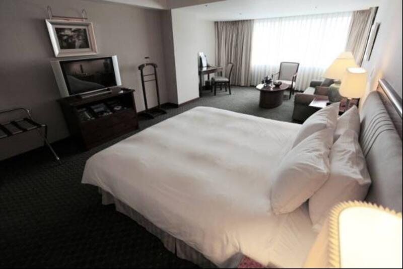 Evergreen Laurel Hotel - Тайчжун Экстерьер фото The photo shows a hotel room featuring a large bed with white bedding. There is a flat-screen television on a wooden cabinet opposite the bed. Nearby, there are two armchairs and a small table, creating a cozy seating area. Large windows allow natura