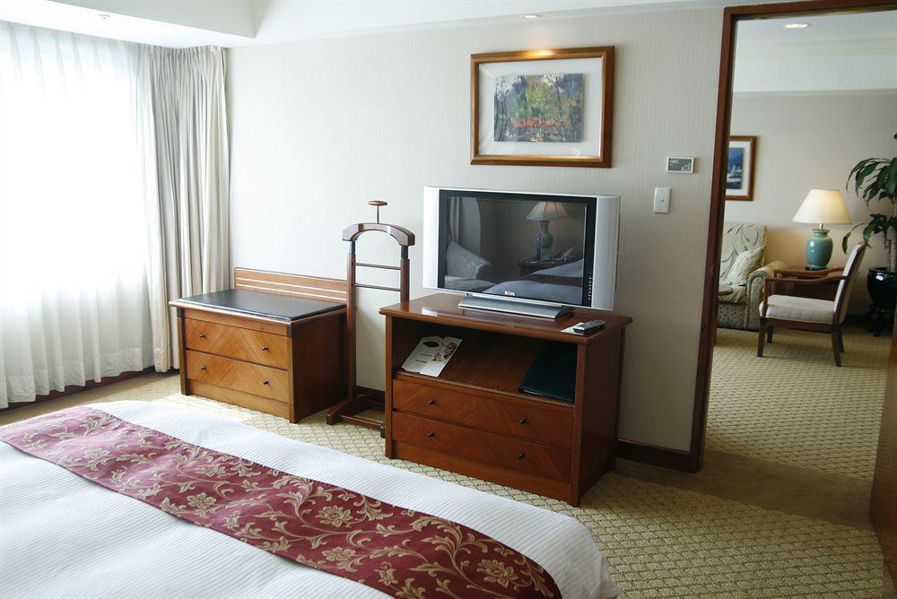 Evergreen Laurel Hotel - Тайчжун Экстерьер фото The photo depicts a hotel room interior. In the foreground, there is a neatly made bed with a decorative red bedspread. To the left, a large window allows natural light to fill the room, with light-colored curtains drawn to one side. 

Next to the be